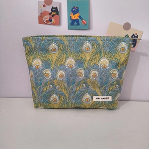 Detail of floral makeup bag with peacock feather pattern and brand tag on white surface