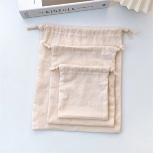 Three sizes of cotton drawstring bags stacked on a white table with Kinfolk book