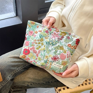 Detail of floral embroidery on a large makeup bag held against casual clothing
