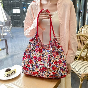 Dettaglio di borsa tote in tela a fiori con manico in corda rossa ed etichetta logo