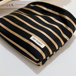 Close-up of a striped satin makeup bag with gold and black bands and brand logo