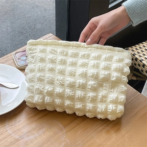 Detail of cream bubble fabric texture on a soft quilted makeup bag over a wooden table