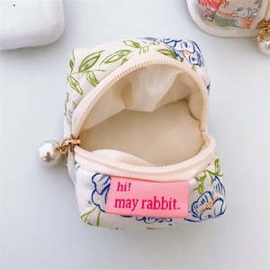 Detailed view of floral earphone pouch featuring a pink fabric label and a pearl zipper pull