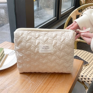 Detail of cream quilted makeup bag with heart stitching on a wooden table setup