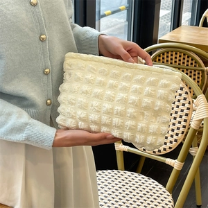 Detail of cream popcorn fabric texture on a soft quilted makeup bag held by hand
