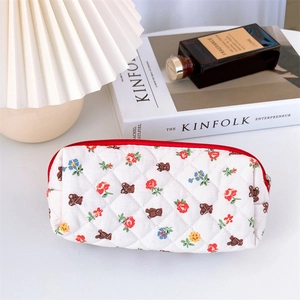 Quilted floral makeup bag with brown bear pattern and red zipper on a white desktop