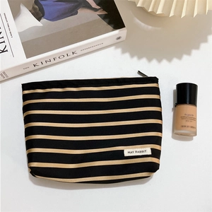 Black and gold striped satin makeup bag with zipper and May Rabbit label on white desk