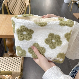 Close-up of plush white makeup bag with green flower pattern and metal zipper detail
