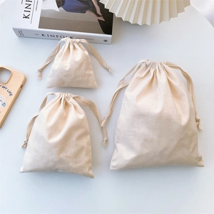 Three sizes of natural beige canvas drawstring bags arranged on a minimalist white desk