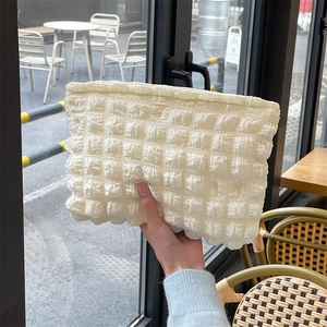 Detailed texture of white quilted bubble cloud cosmetic bag held in hand outdoors