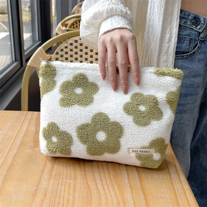 Close-up of plush floral makeup bag with green flower patterns and brand label on a desk