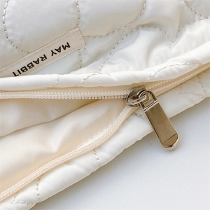 Close-up of white quilted fabric detailing with metal zipper and woven brand label