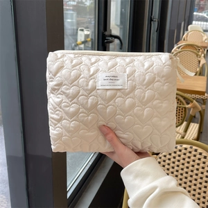 Quilted cream vanity bag with heart stitching and zipper closure in outdoor setting