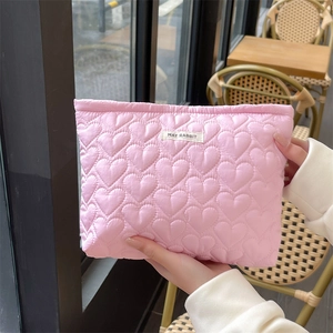 Detail of pink quilted cosmetic bag featuring heart pattern embroidery and soft texture