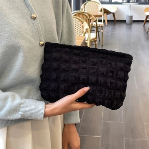 Detail of a black bubble texture pouch held by a model in a cozy indoor setting