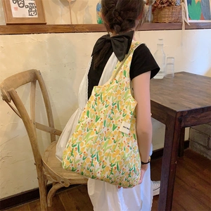 Détail du sac cabas en toile avec imprimés floraux jaune et vert et étiquette de marque