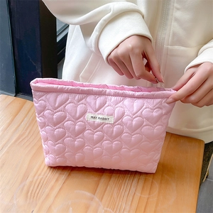 Close-up of pink quilted heart makeup bag with zipper closure and brand label detail