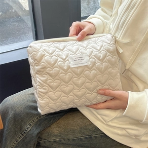 Detail of cream quilted makeup bag with heart pattern held in hands for daily use