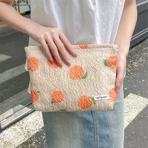 Detail of floral jacquard makeup bag with orange embroidery and brand woven label