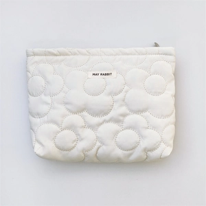 Close-up of white quilted floral makeup bag with rectangular woven label and zipper