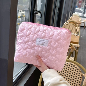 Close-up of pink quilted heart makeup bag with zipper and logo held by a model