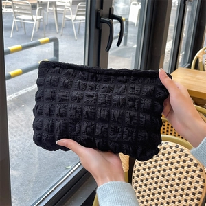 Close-up of black bubble textured puffy makeup bag held by a model in a cozy cafe setting