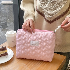 Detailed pink quilted makeup bag with embossed heart patterns on a wooden table