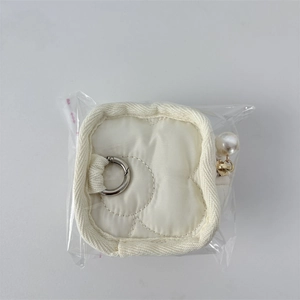 Close-up of quilted cream pouch with floral stitching, metal ring, and large faux pearl