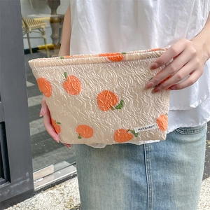 Detail of cream jacquard makeup bag with orange fruit pattern and brand label