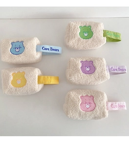 Détail de cinq pochettes en peluche Care Bears avec broderies colorées et texture douce