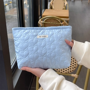 Detailed shot of light blue quilted heart pattern cosmetic bag with a small woven label