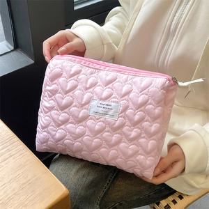 Close-up of pink quilted heart pouch with brand label held by a hand in warm light