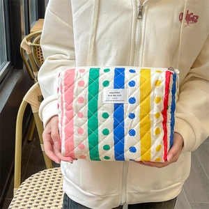 Close-up of quilted colorful striped zipper pouch held by a person in a white hoodie