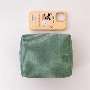 Green corduroy cosmetic bag detail showing ribbed texture with phone case for scale