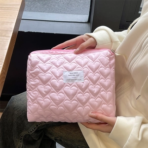 Detailed view of hand-held pink quilted heart cosmetic bag with logo patch and top zipper
