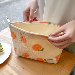 Detailed view of embossed orange jacquard makeup bag with gold zipper and brand label