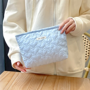 Close-up of light blue quilted heart texture and brand tag on a soft cosmetic bag