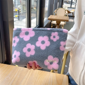 Cute gray plush makeup bag with pink floral patterns held in a lifestyle cafe setting