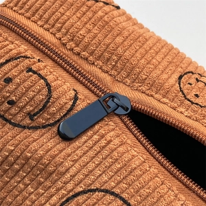 Close-up of brown corduroy cosmetic bag with embroidered smiley face and metal zipper