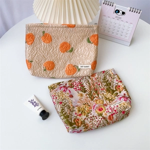 Detail of jacquard makeup bags featuring orange patterns and brand tags on a white table