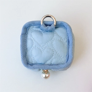 Détail d'une pochette matelassée bleu clair en forme de cœur avec perle et anneau