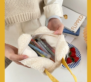 Détail de la capacité intérieure de la trousse en peluche avec stylos et poignée jaune