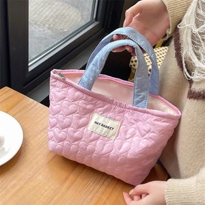 Detail of pink quilted tote bag with heart pattern and contrast blue handles on wooden table