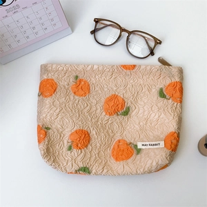 Flat lay of textured jacquard makeup bag with orange pattern near a calendar and glasses
