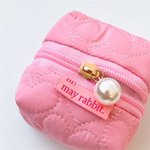 Détail de la pochette matelassée rose avec perle sur zip et étiquette de marque rouge