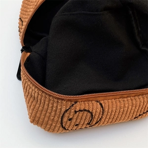 Macro shot of brown corduroy makeup bag detailing smiling face print and inner canvas lining