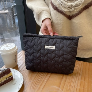 Detail of black quilted heart texture makeup bag held by hand in a cozy cafe setting