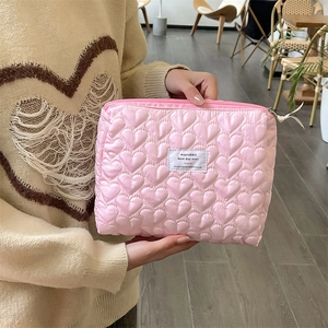 Close-up of pink quilted heart makeup bag with white label held by a person