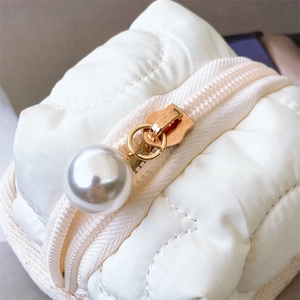 Macro shot of cream quilted nylon earphone pouch featuring a large pearl zipper charm