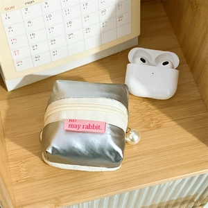 Macro shot of silver metallic padded pouch with zipper pearl charm and brand label